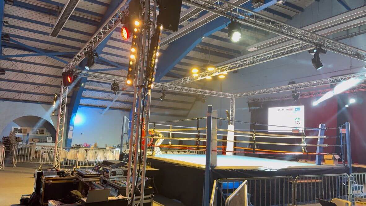 Vue d’ensemble du ring de boxe éclairé avec panneaux sponsors et tribunes